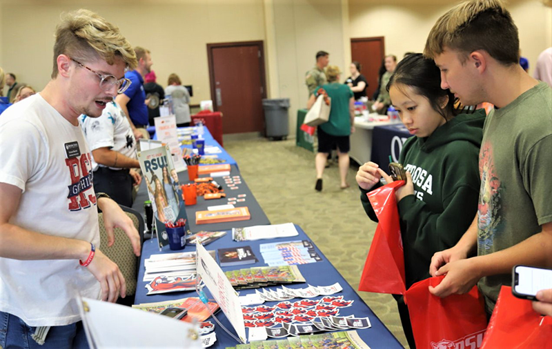 Students walking through college fair visiting tables of info.