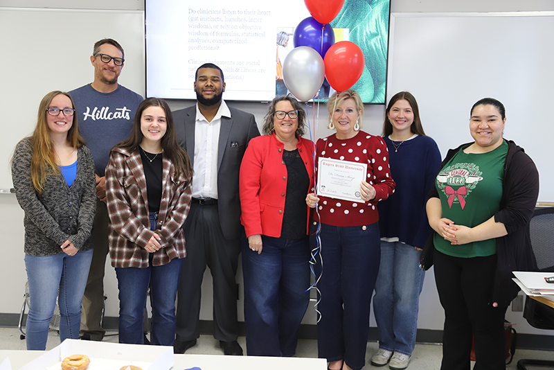 Group of people posing with woman holding certificate and balloons