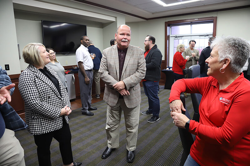 Group of people standing around celebrating man retiring.