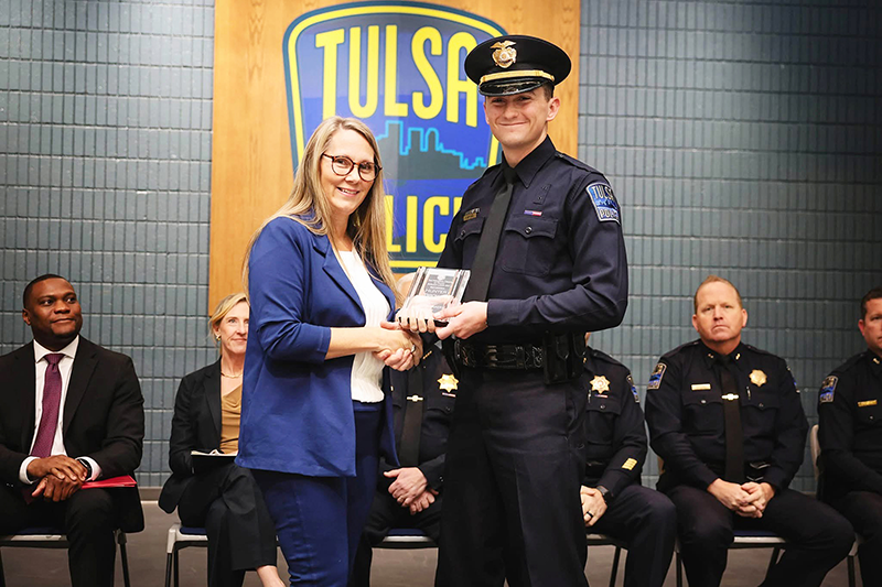 Woman shaking hands with and holding an award with a police officer.