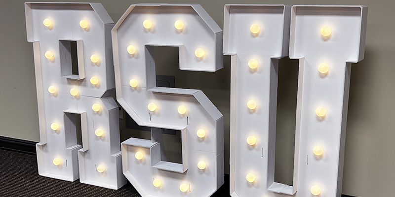 Large stand-up white R-S-U letters with light bulbs around their edges