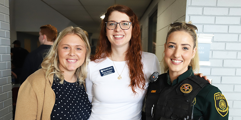 Three females pose together and smile at the camera.