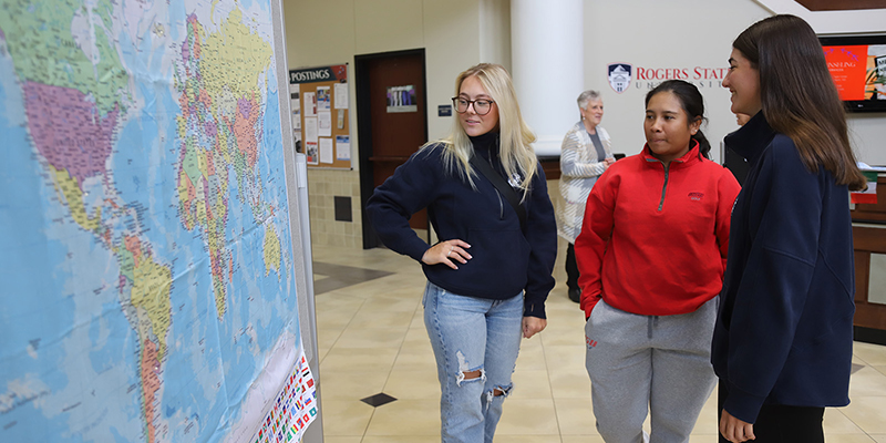 Three students talk while looking at a world map