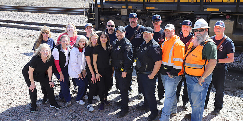 A group of adults pose together outdoors in front of a train.